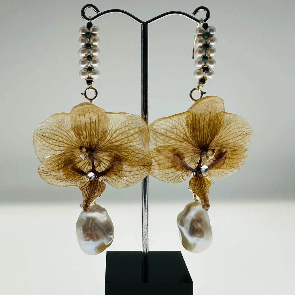 Brown floral earrings with pearl-like droplets on a stand against a gray background
