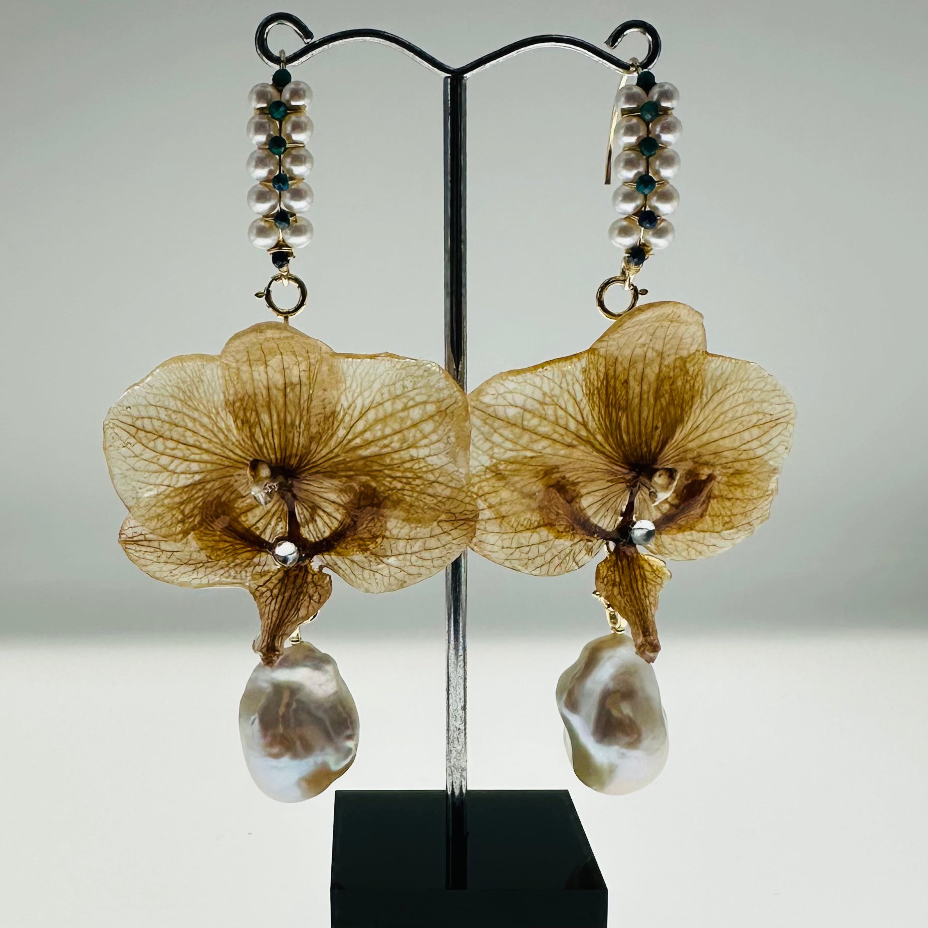 Brown floral earrings with pearl-like droplets on a stand against a gray background