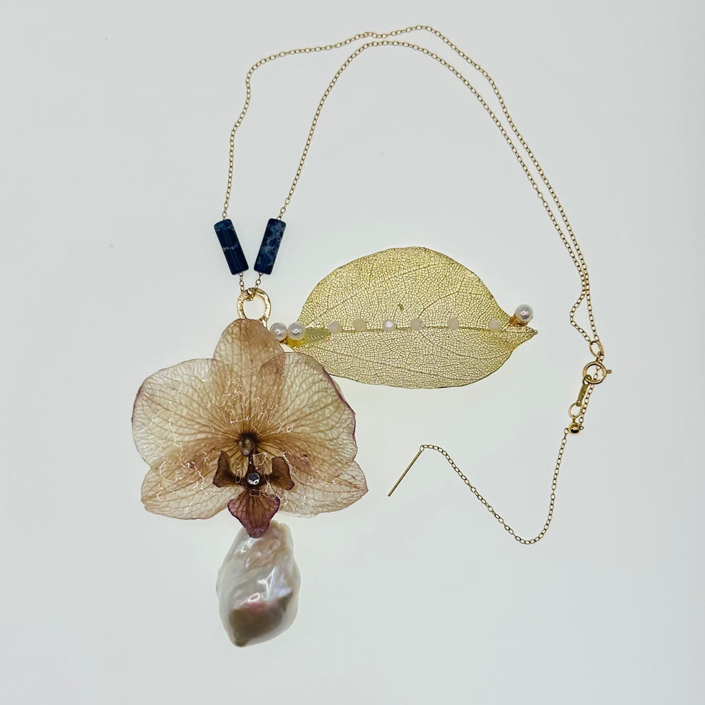 Necklace with dried flower, leaf, and pearl pendant on a light background